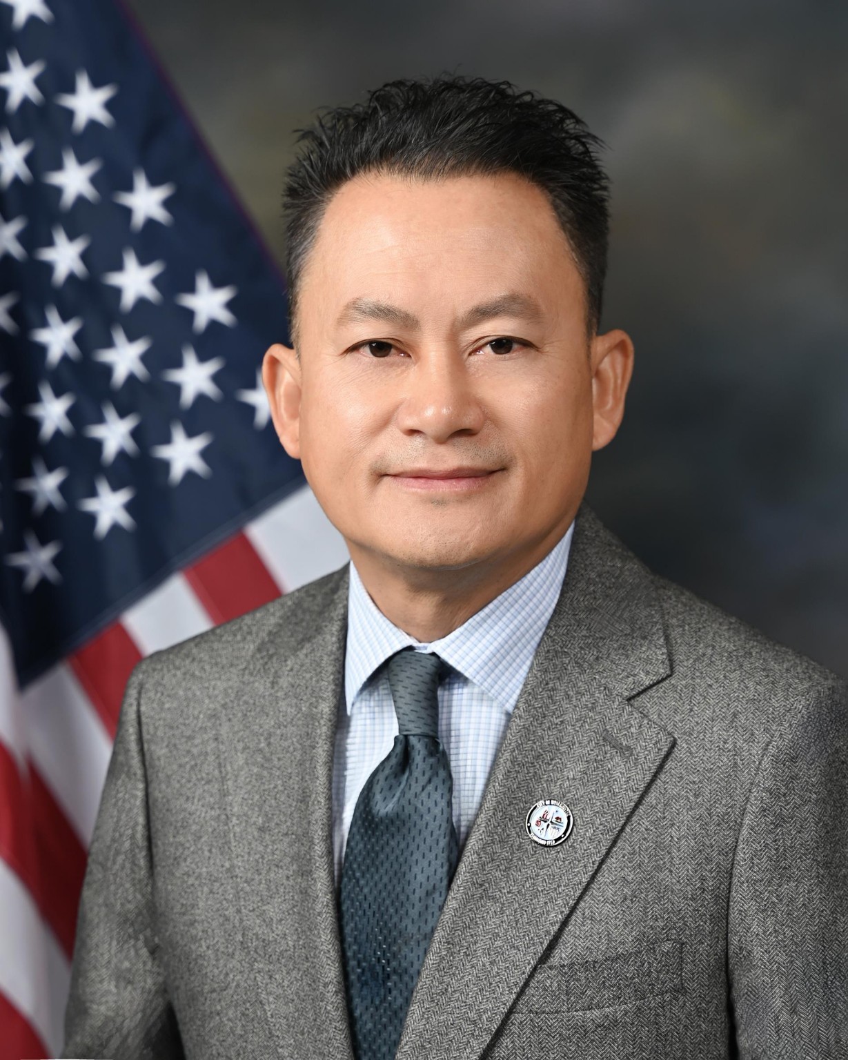 Formal portrait of Mark Nguyen wearing a gray suit with an American flag in the background